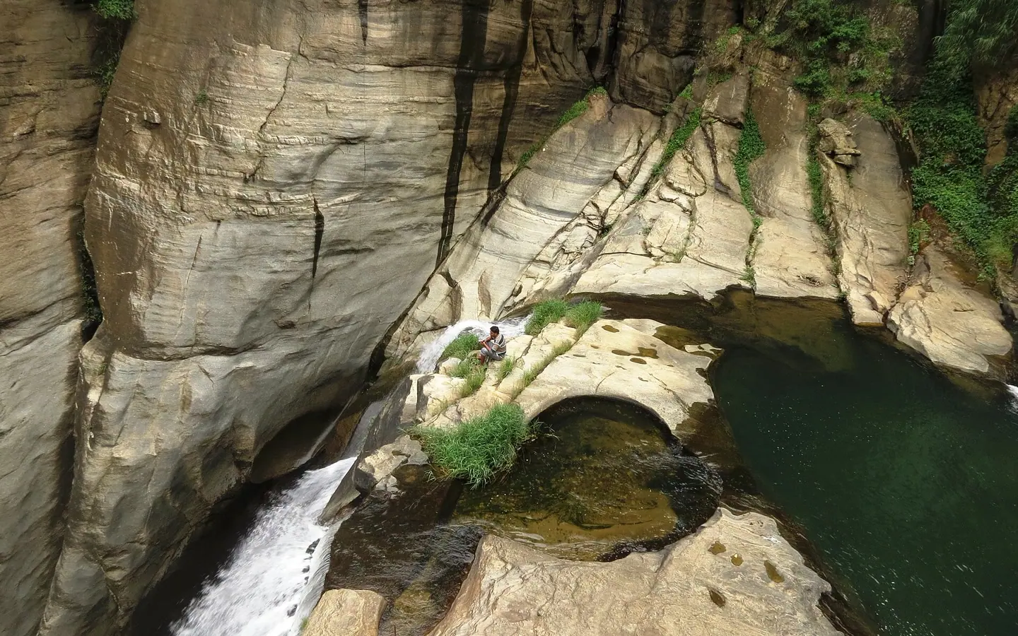 Wide contextual view of rock pools above Ravana Ella with a local person seated at a distance